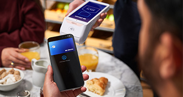 Contactless card payment at a café table using a handheld card reader during a casual dining experience