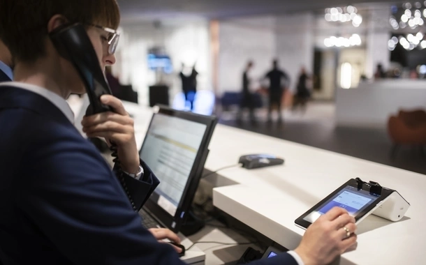 At the reception desk of Elavon customer Nosalowy Dwór Resort and Spa, a receptionist holds a phone to their ear. A payment terminal and computer monitor are on the desk