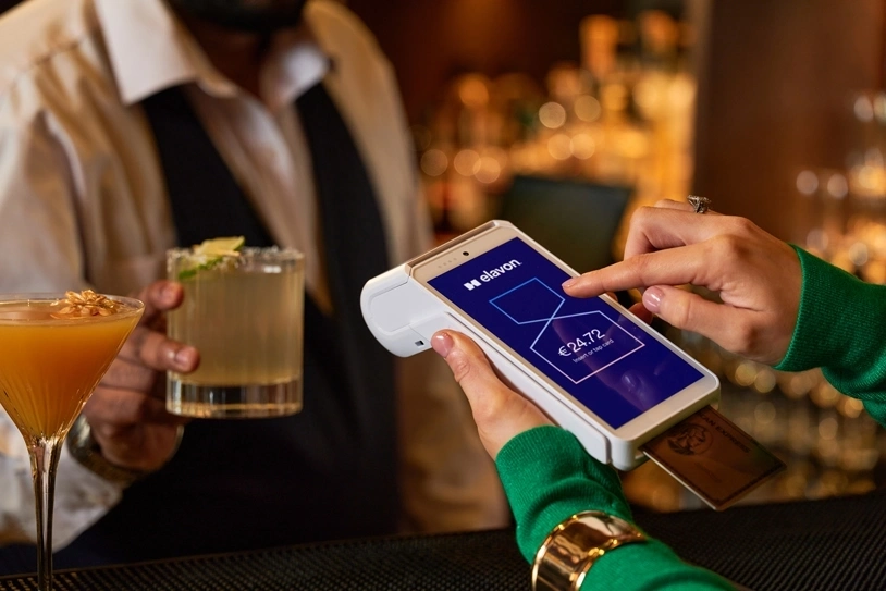 Contactless card payment at a bar using a handheld POS terminal while bartender serves cocktails